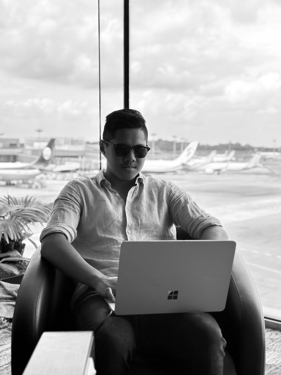 Zach in an airport lounge, working on a laptop, with parked aircraft behind the glass.